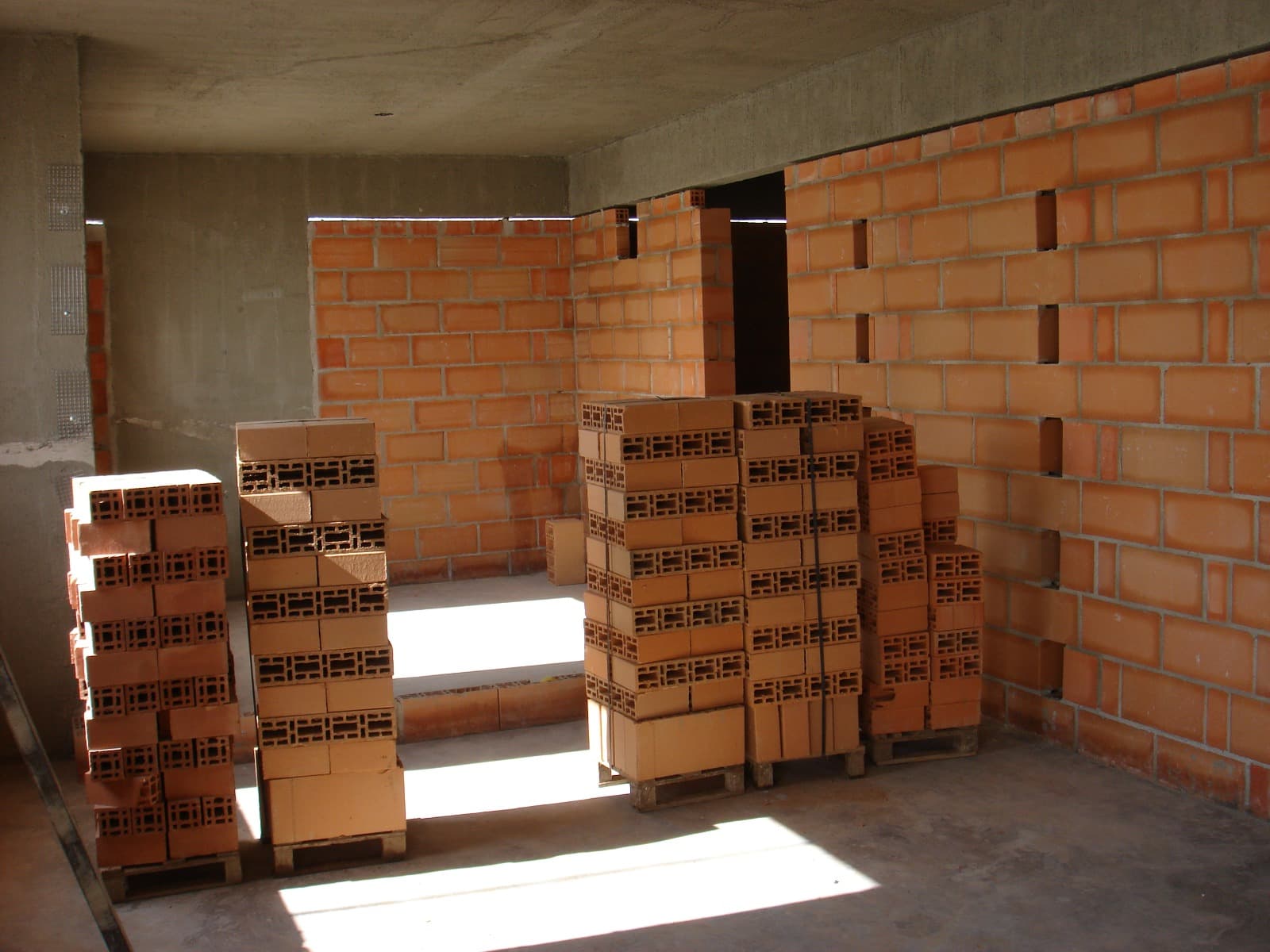 Blocos cerâmicos empilhados no interior de uma estrutura em obra, iluminados por luz natural