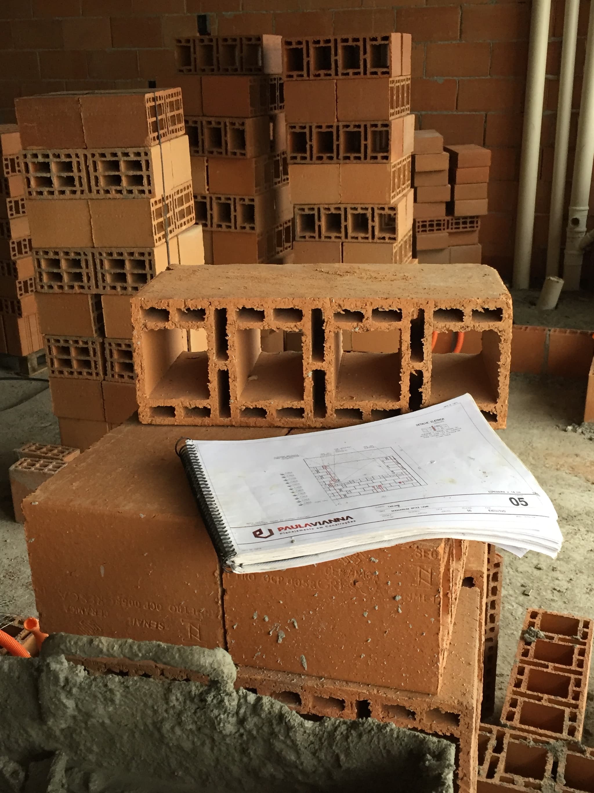 Caderno de projeto de vedação da Paula Vianna apoiado sobre blocos cerâmicos no canteiro de obras